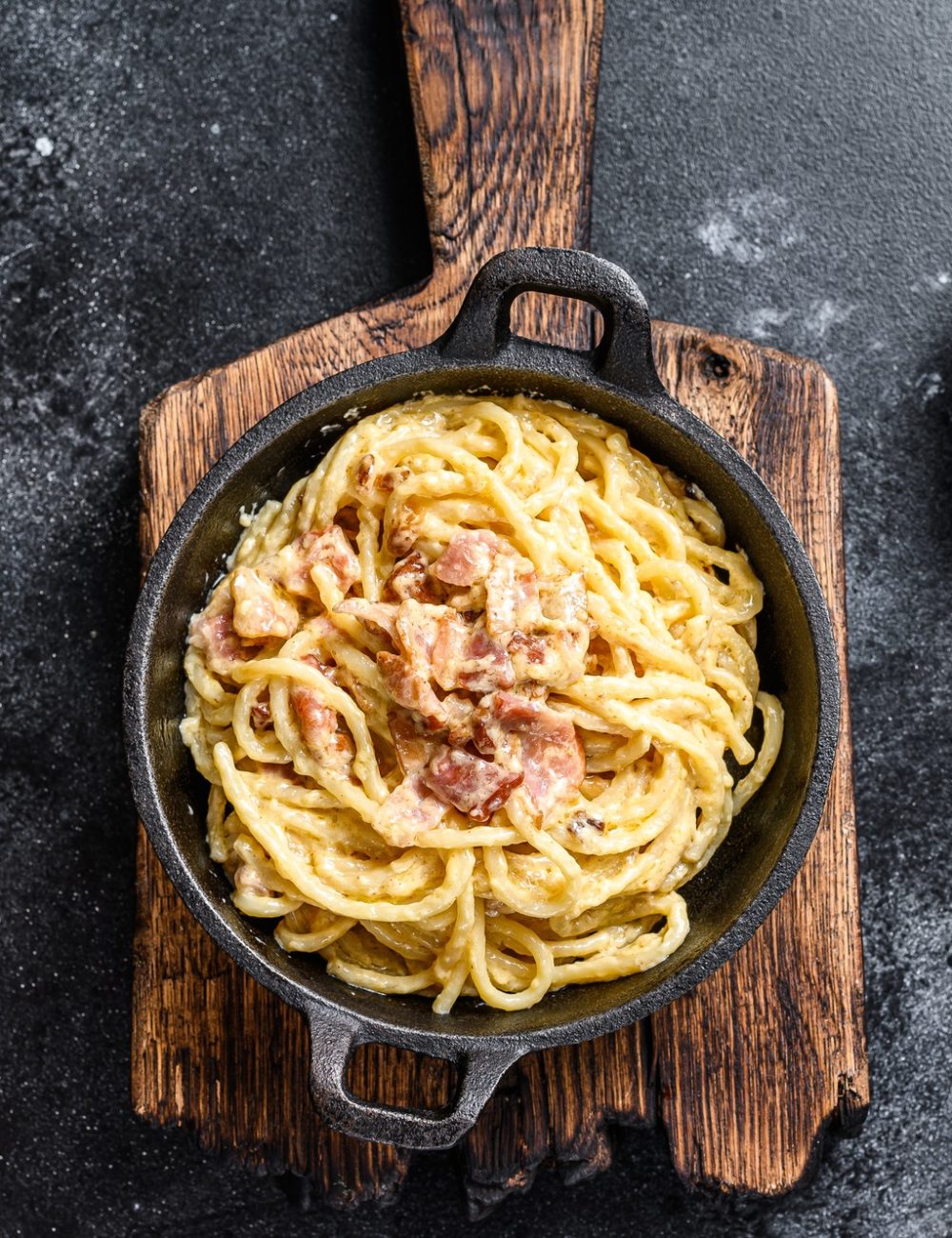 Pasta Carbonara with bacon and parmesan in a pan. Black background. top view